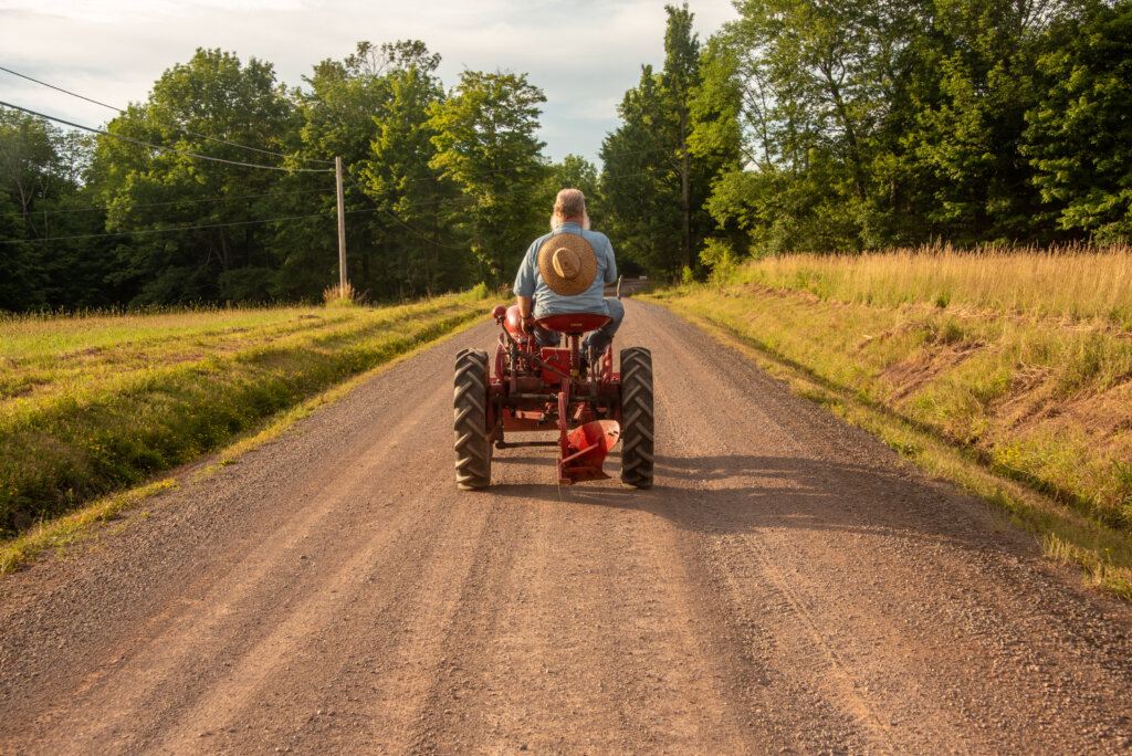 Farmer rides down dirt road on small tractor